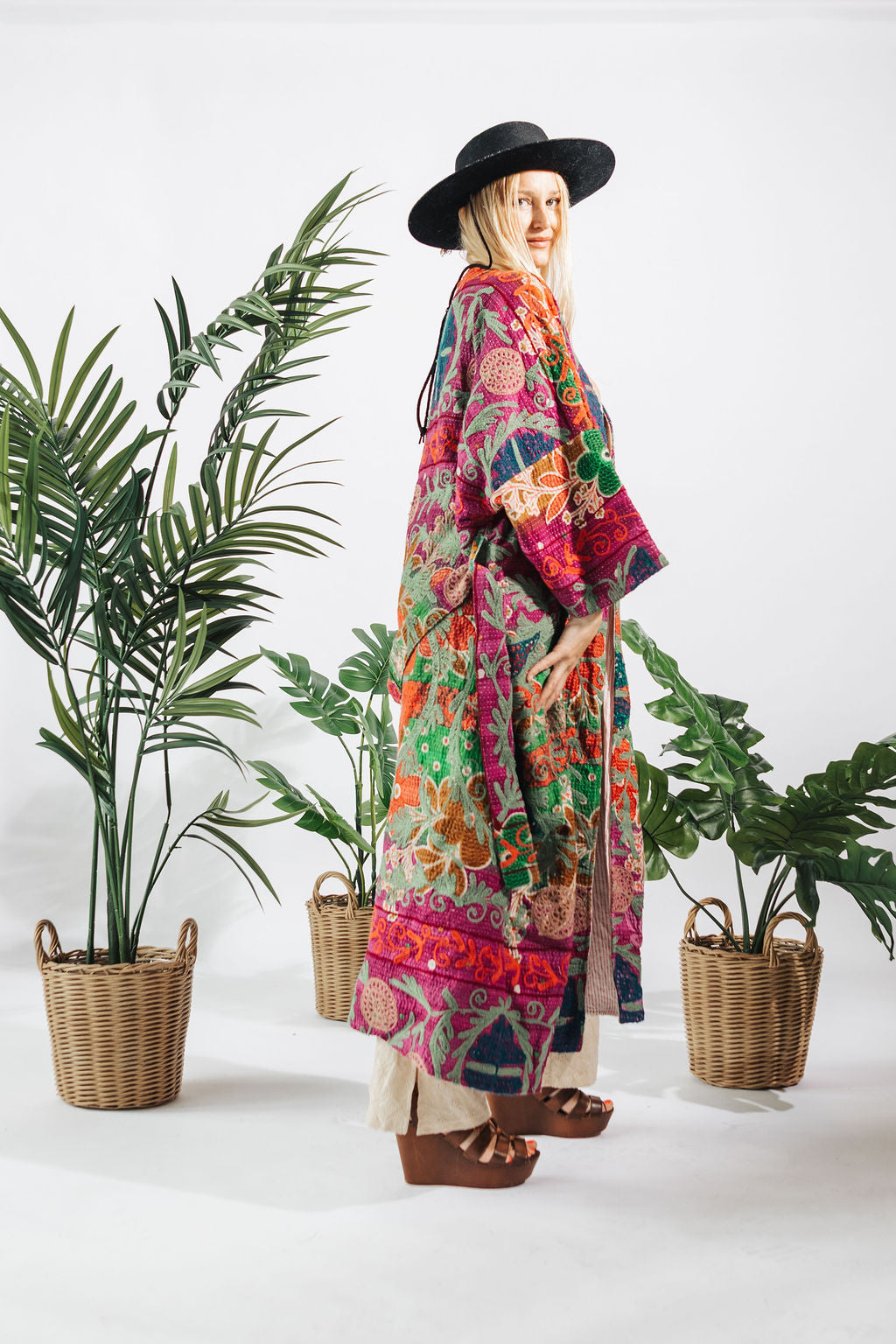a woman in a colorful robe and hat standing in front of plants