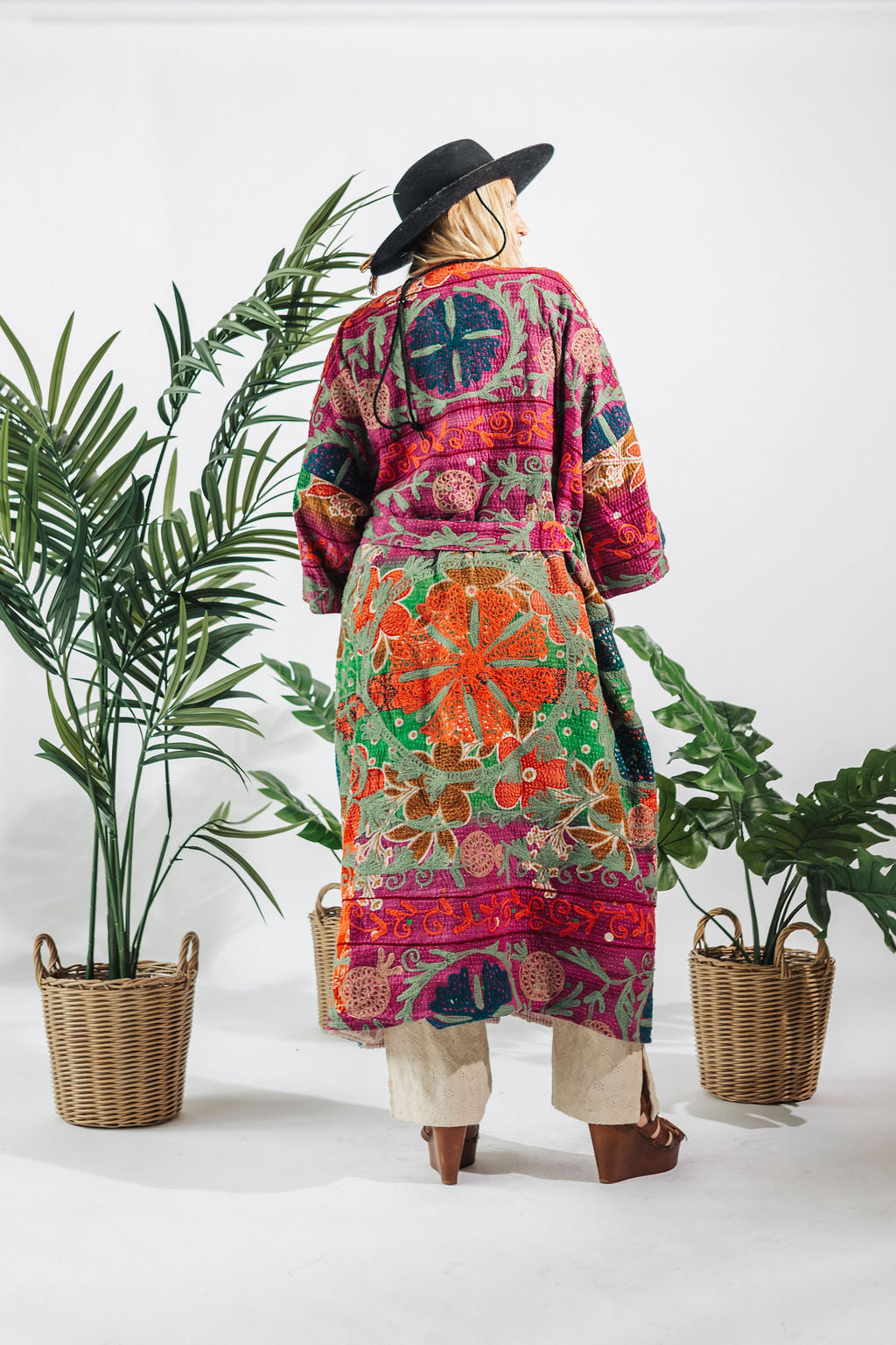 a woman in a colorful robe and hat standing next to two baskets of plants