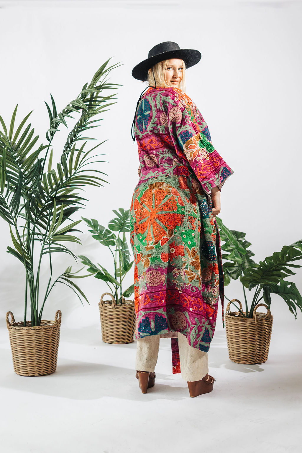 a woman in a colorful robe and hat standing next to plants