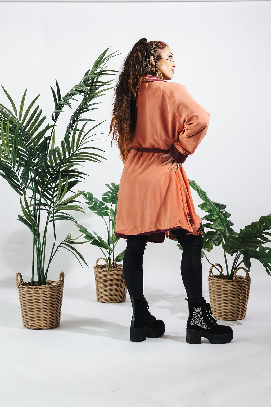 a woman in a pink dress and black pants standing next to two baskets of plants