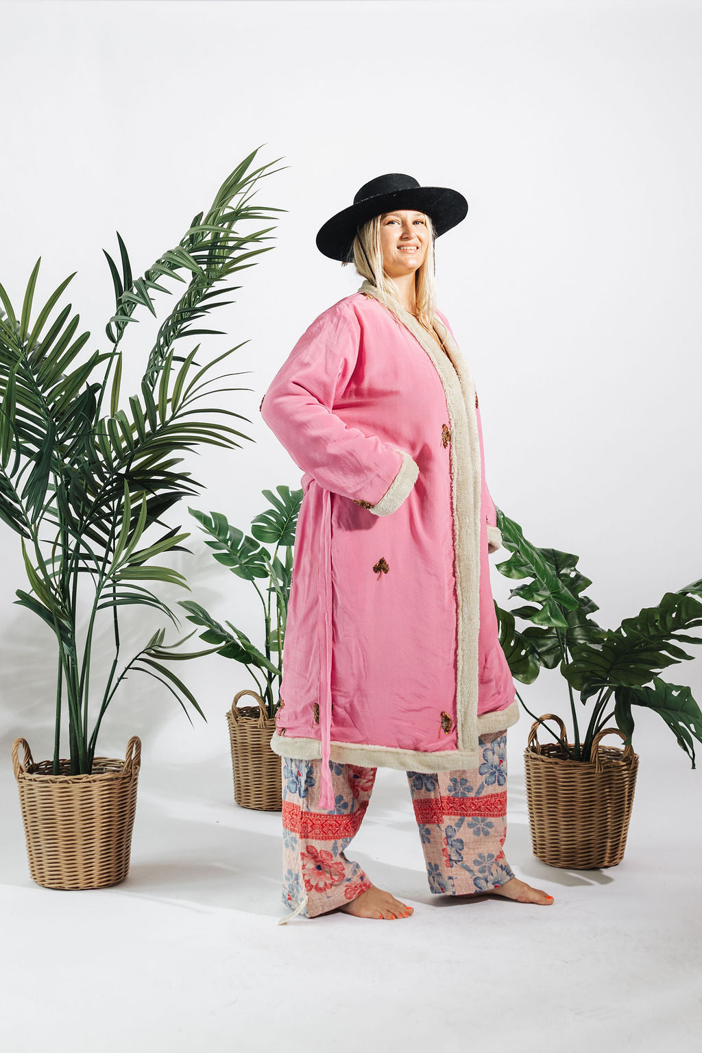a woman in a pink robe and hat standing next to plants