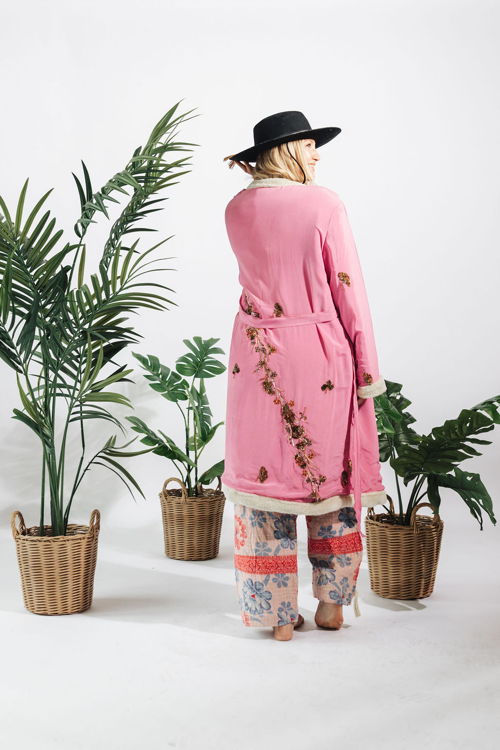 a woman in a pink robe and hat standing next to plants