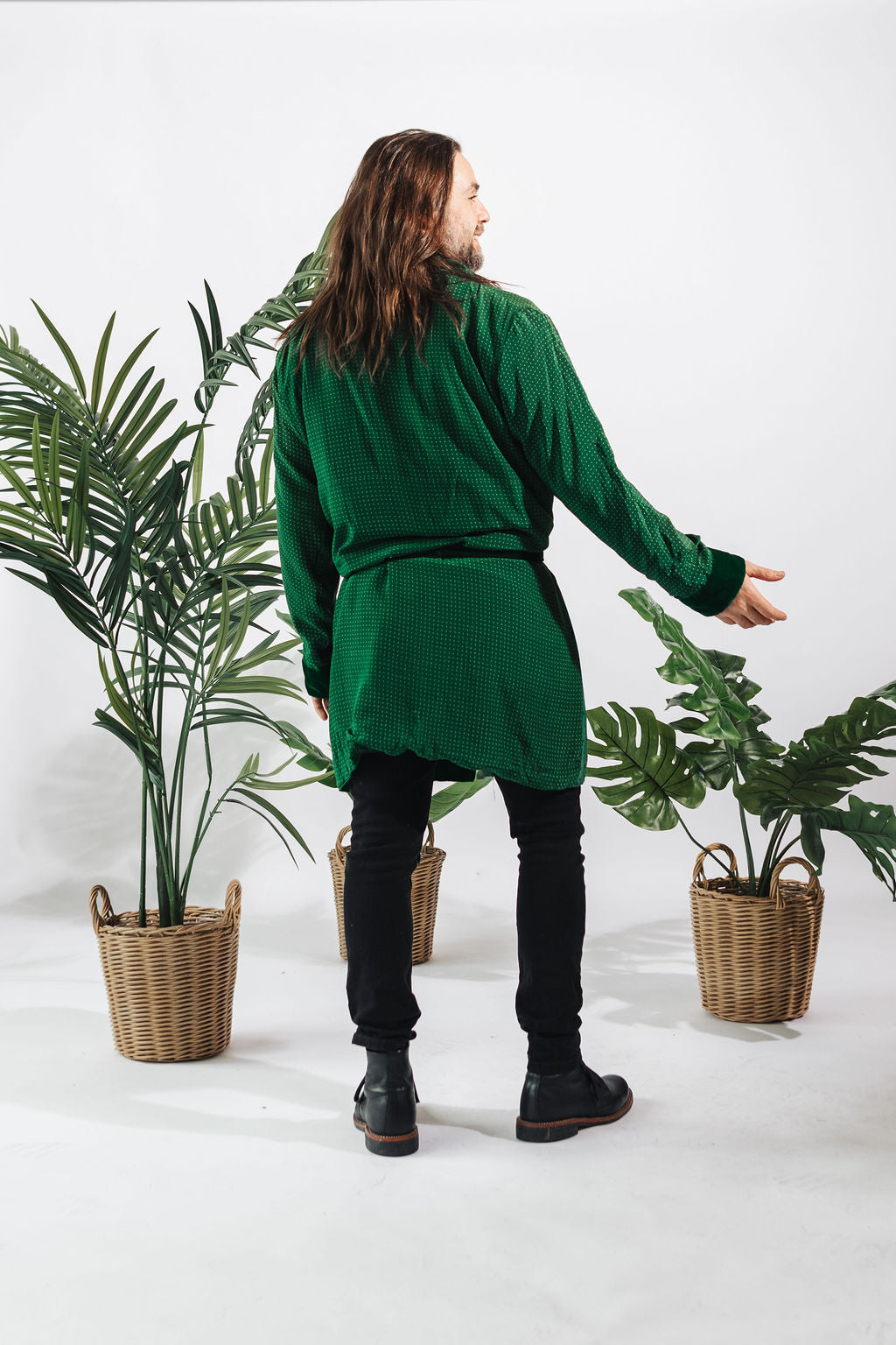 a man in a green shirt and black pants standing next to two plants