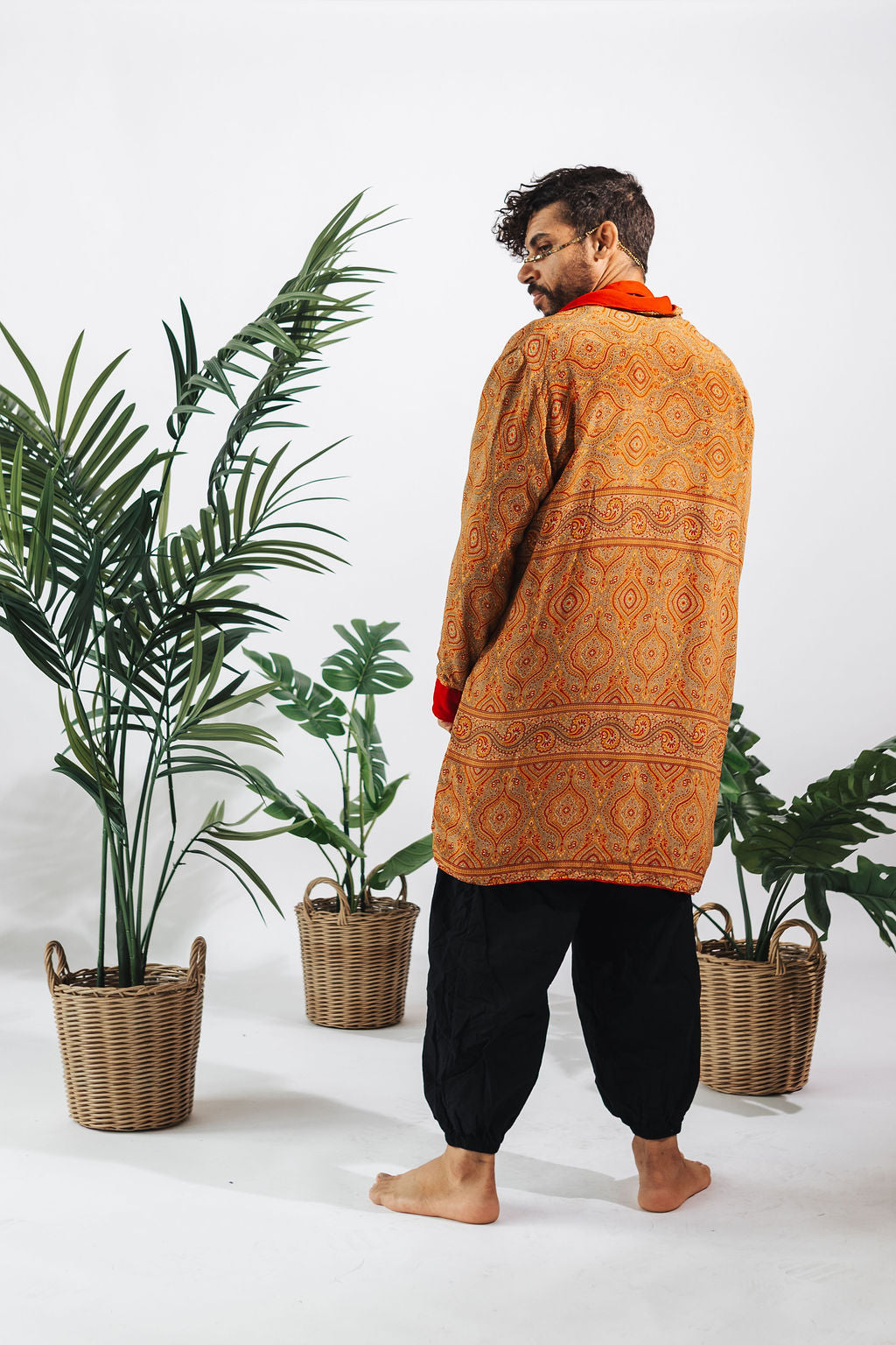 a man in a long orange shirt and black pants standing next to two baskets of plants