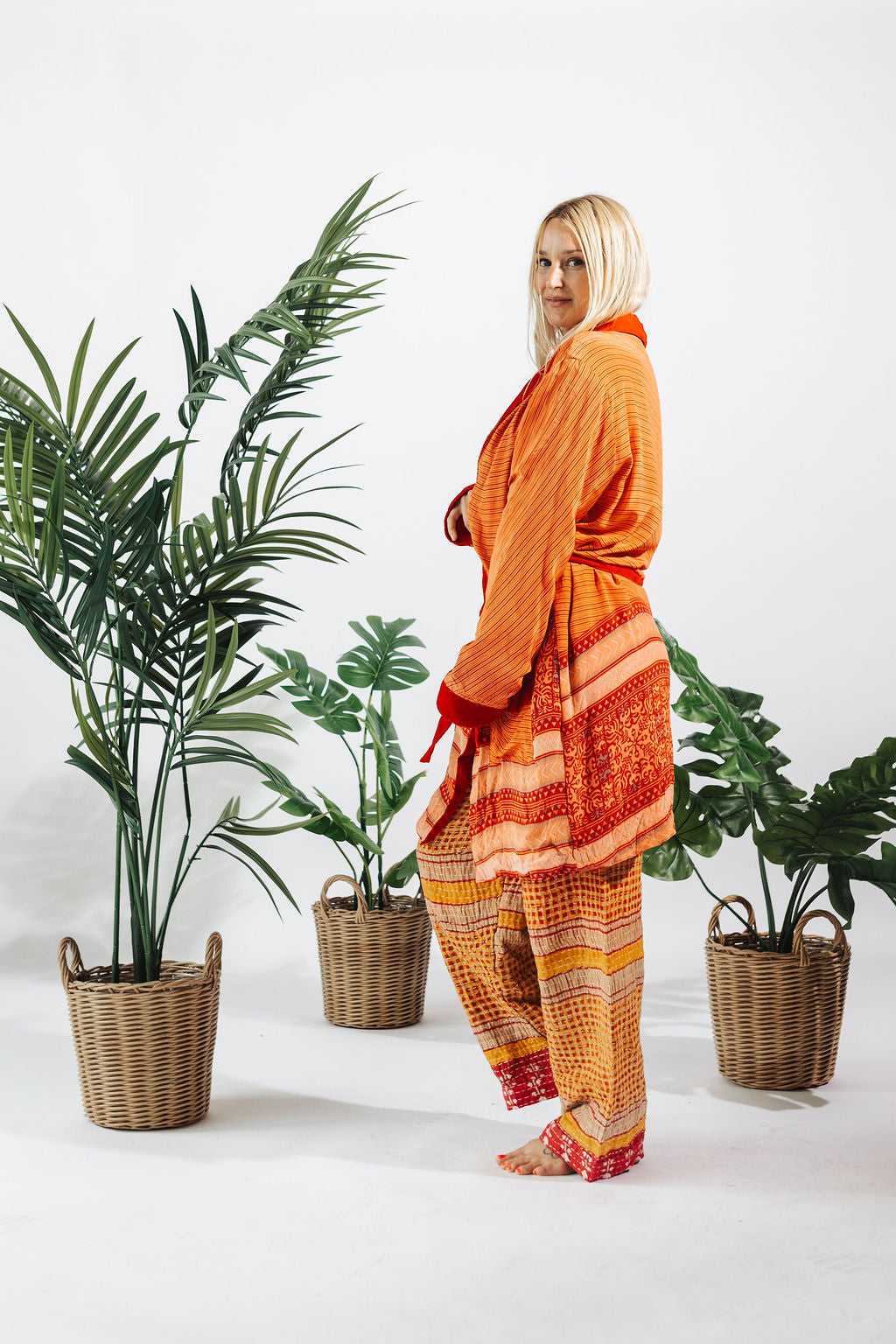 a woman in orange robe and orange pants standing next to plants
