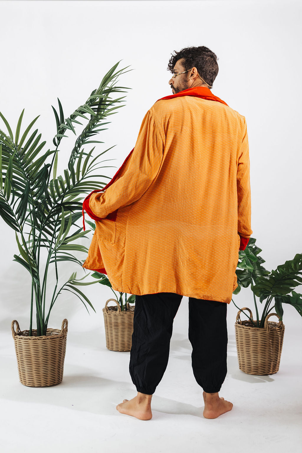 a man in an orange robe standing next to a plant