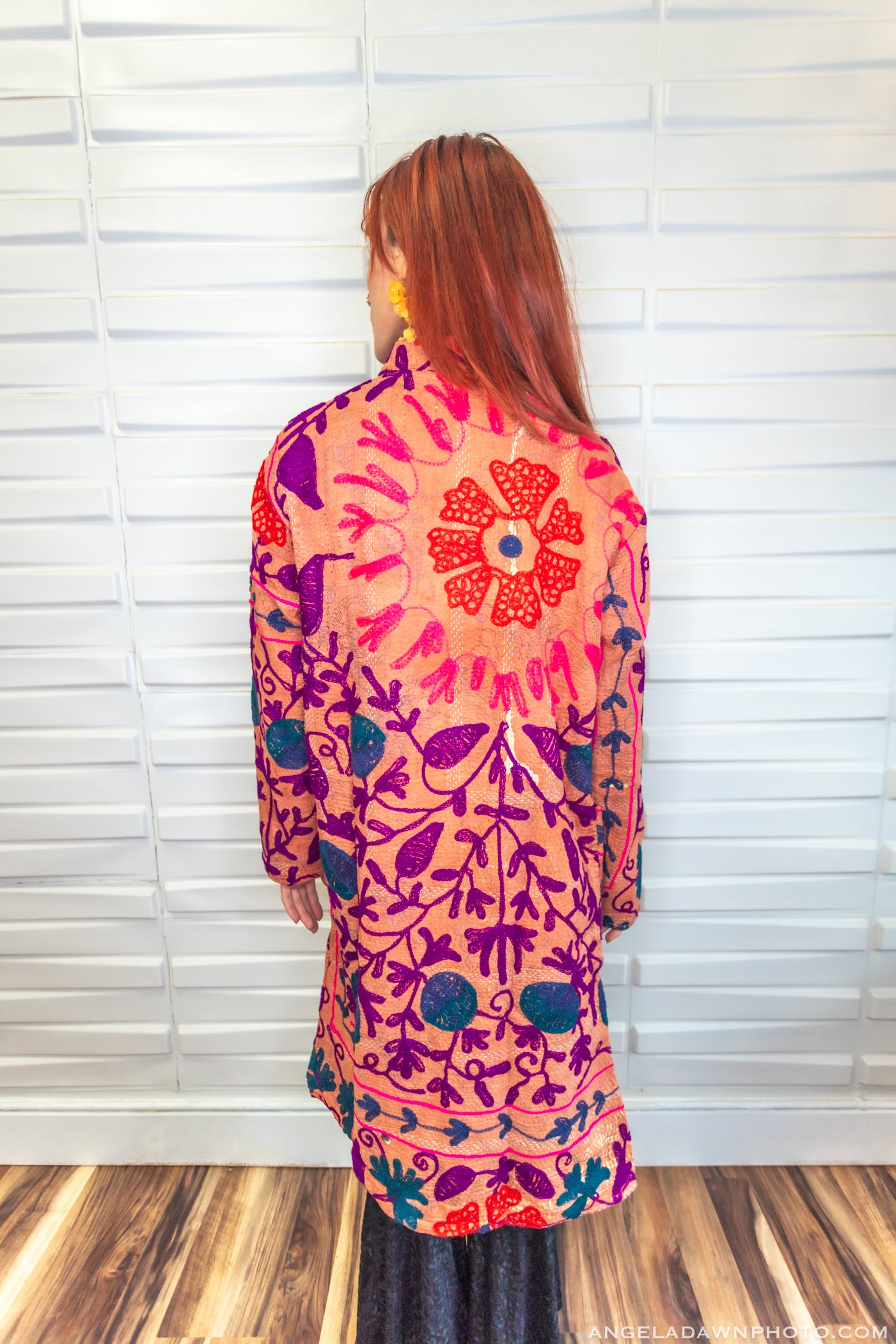 Woman wearing a colorful patterned dress standing against a white wall.