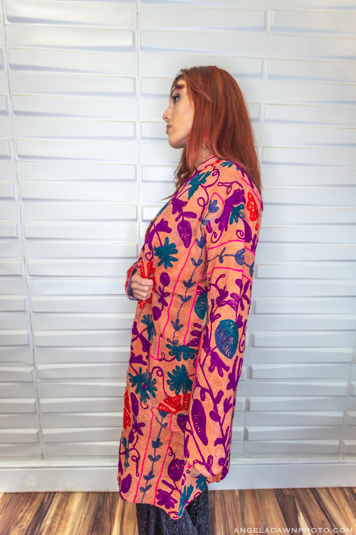 Woman wearing a colorful patterned shirt against a white paneled wall.