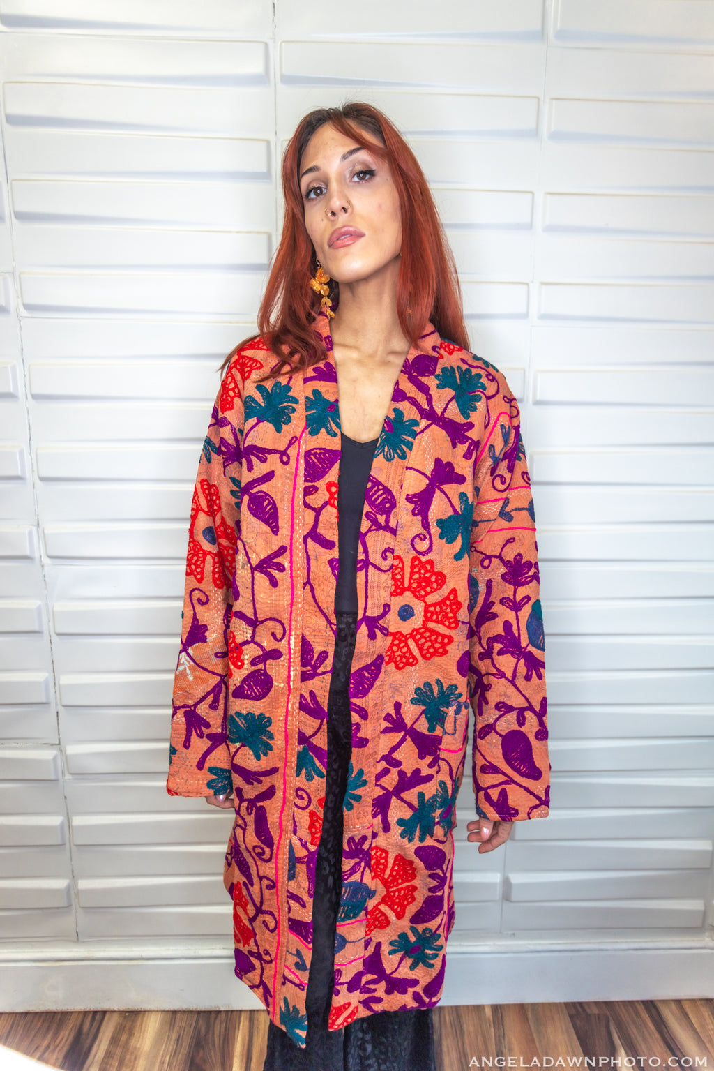 Woman wearing a colorful patterned coat standing against a white wall.