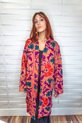 Woman wearing a colorful patterned coat standing against a white wall.