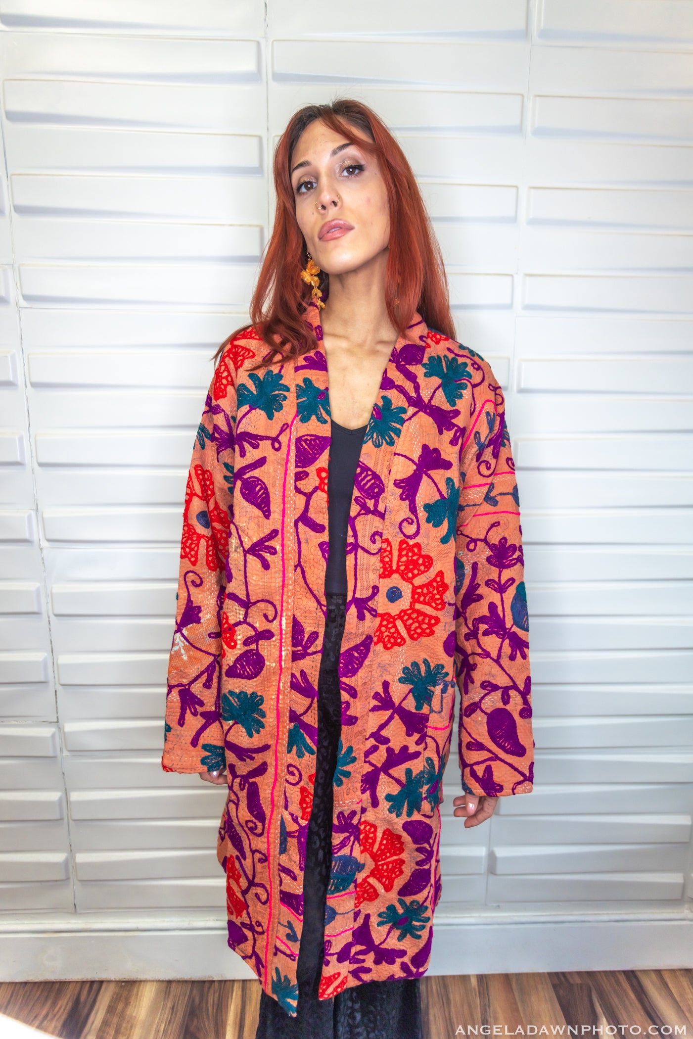 Woman wearing a colorful patterned coat standing against a white wall.
